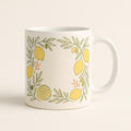 Hero shot of a white ceramic mug with a hand-drawn lemon and olive branch border on a plain background