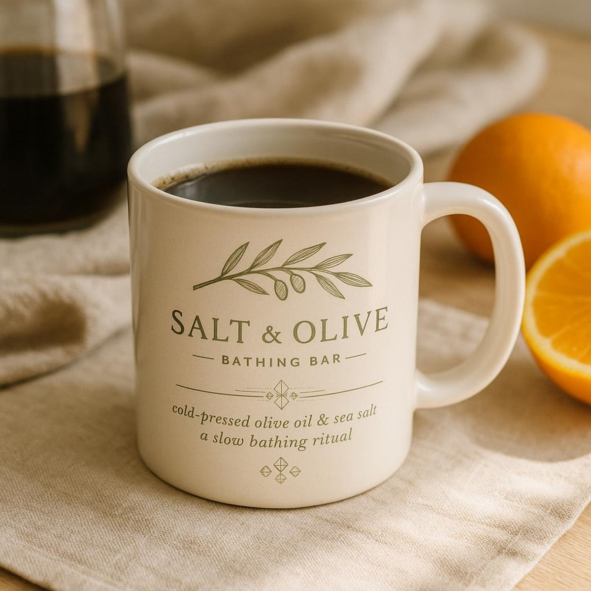 Lifestyle scene of the Salt and Olive mug on a wooden kitchen table with morning coffee