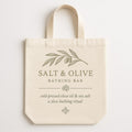 Natural ecru cotton tote bag printed with olive branch and sea salt design, shown flat against a pale background