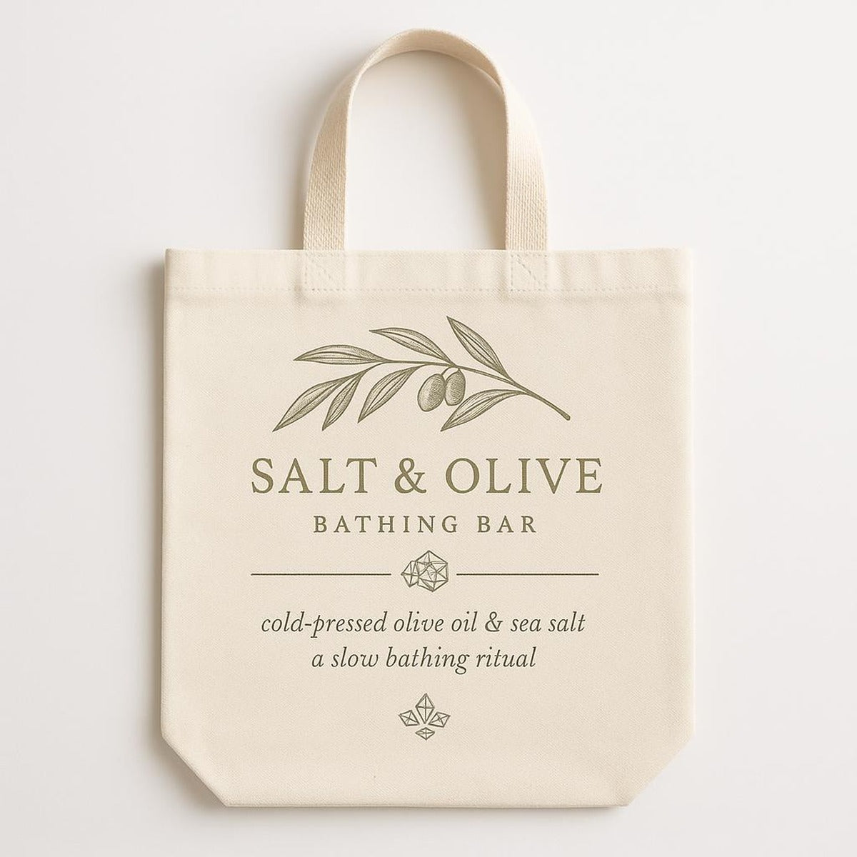 Natural ecru cotton tote bag printed with olive branch and sea salt design, shown flat against a pale background