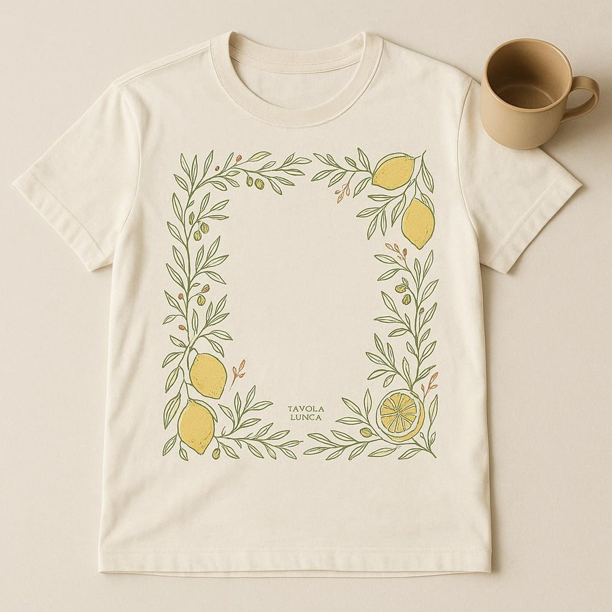 Folded cream tee beside a lemon and olive sprig to show print scale and fabric texture