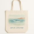 Hero shot of a sea-glass green canvas tote bag with a subtle tonal slow down coastal motif near the base
