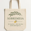 Natural cotton tote bag printed with a rustic ceramic carafe in coastal blue glaze, shown flat on a linen backdrop