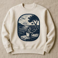 Olive green sweatshirt printed with a hand-carved olive-wood coffee scoop and clip illustration, shown flat on a linen backdrop