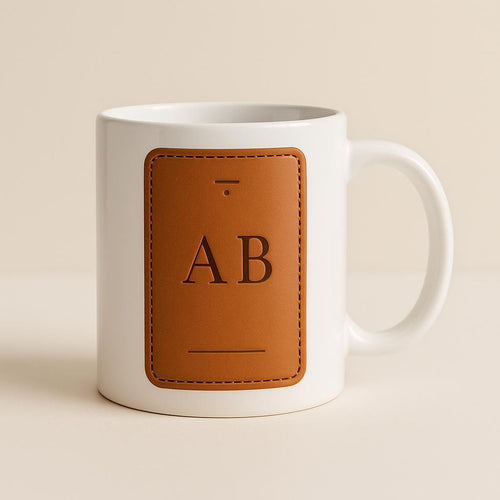 Tan and cream ceramic mug printed with a vegetable-tanned leather luggage tag illustration on a white background