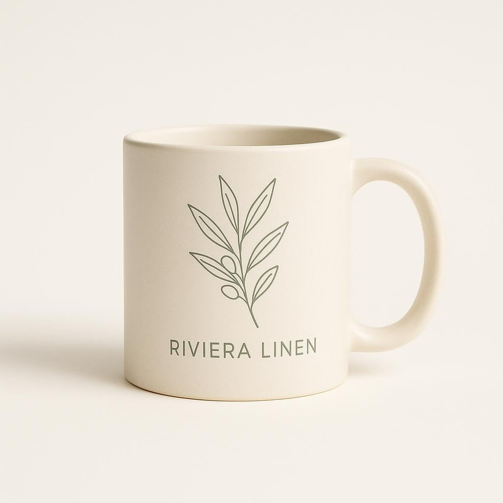 Sand beige ceramic mug with muted Riviera linen shirt illustration on a plain background