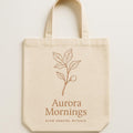 Natural cotton canvas tote bag printed with two matte-glazed Mediterranean breakfast bowls in sand and terracotta tones