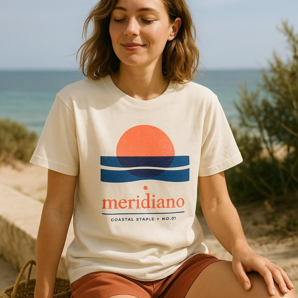 Person wearing the Meridiano cotton tee outdoors near a whitewashed coastal wall in warm afternoon light