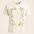 Cream premium cotton t-shirt with a hand-drawn lemon and olive branch border across the chest, laid flat on a linen surface
